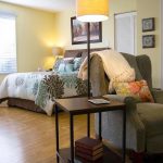 Room with comfy chair, lamp and a bed.