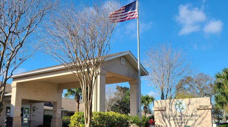 Front entrance side view with flag and Magnolia Gardens sign.