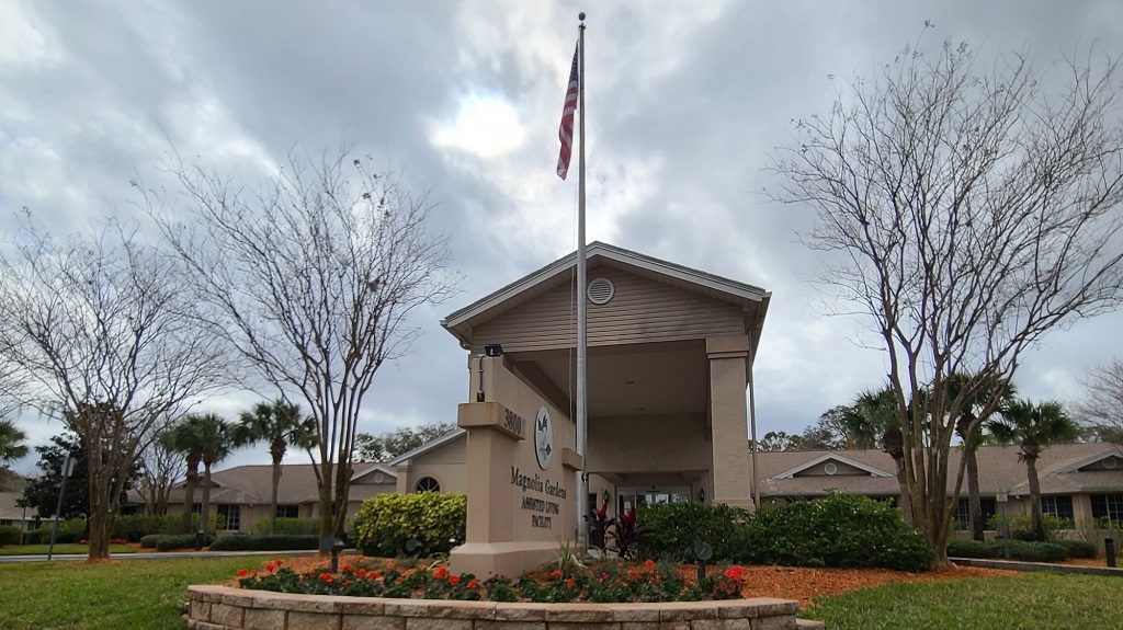 Front of building with flag and flowers.